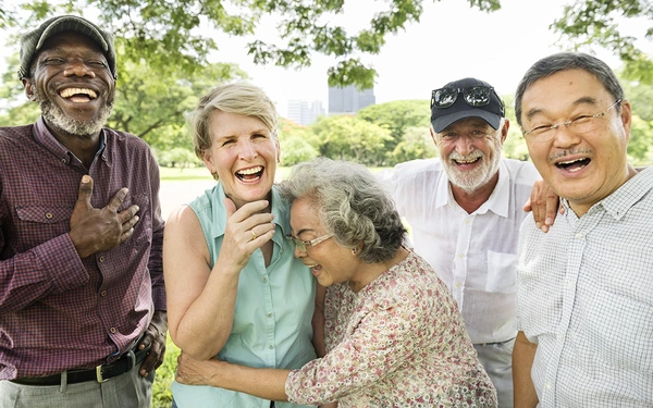 Fünf Senioren lachen und genießen gemeinsam einen entspannten Tag im Park, unterstützt von SHD Systemhäusern.