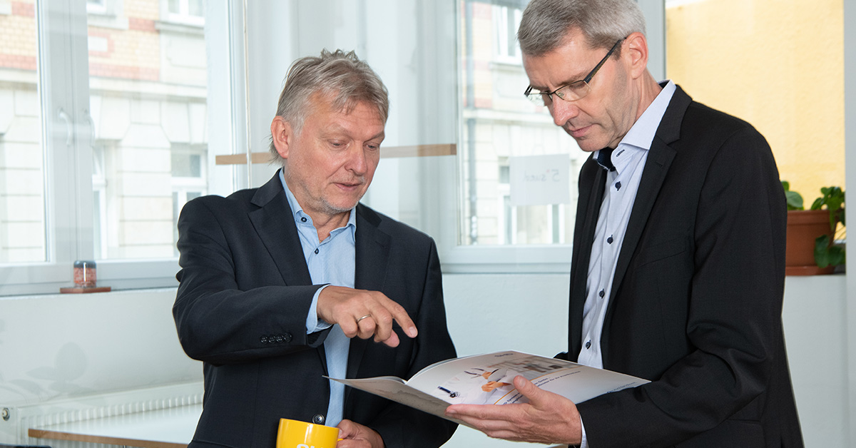 Zwei Geschäftsleute diskutieren über IT-Lösungen von SHD bei Tageslicht in einem modernen Büro.