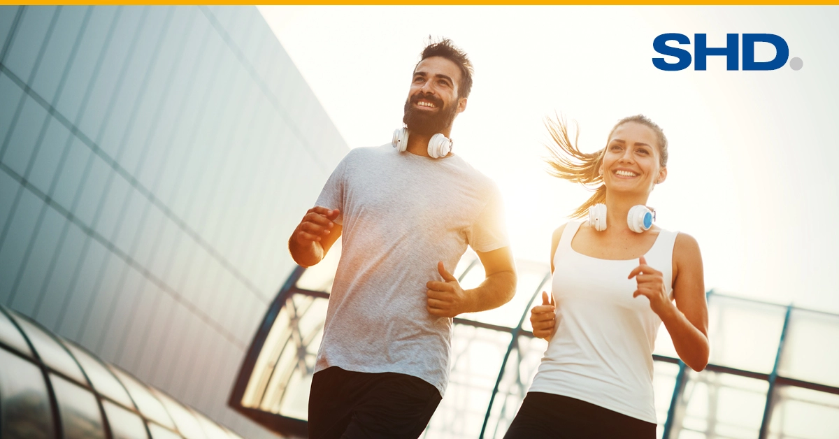 Zwei junge, lächelnde Jogger im Sonnenschein symbolisieren Engagement von SHD für Gesundheit