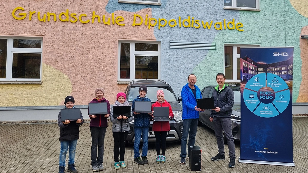 Sechs Kinder halten Laptops vor der Grundschule Dippoldiswalde, unterstützt von SHD IT-Dienstleistungen.