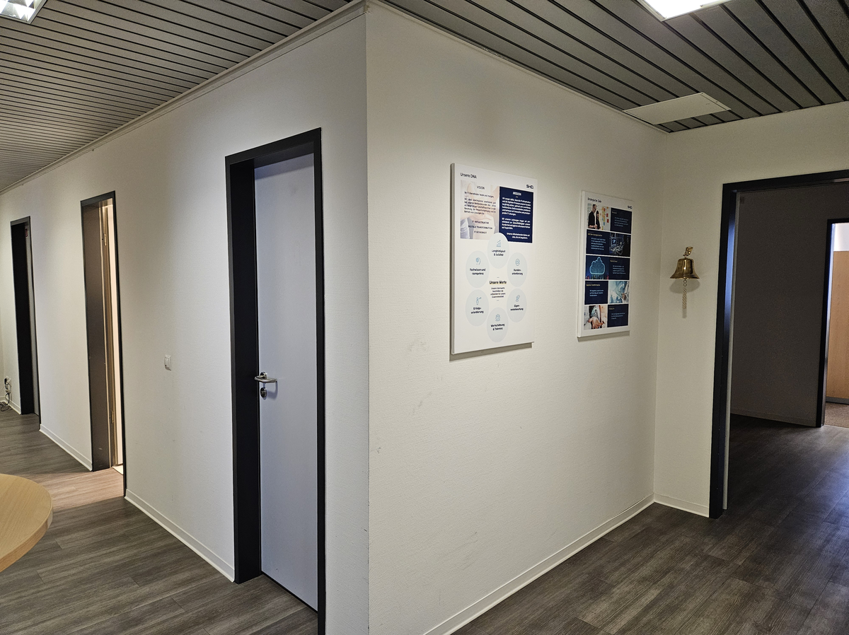 Ein Büroflur mit Türen, Informationsplakaten von SHD und modernem Design in der Hamburger Geschäftsstelle.