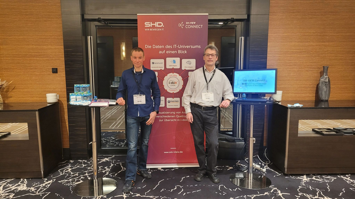 Zwei Personen stehen neben einem Präsentationsstand, der IT-Lösungen von SHD präsentiert.