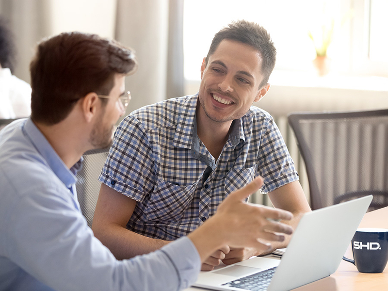 SHD Service-Experte im Beratungsgespräch mit einem Kunden an einem Tisch mit geöffnetem Laptop.