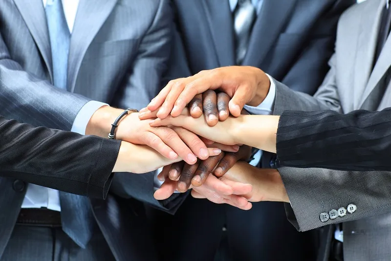 Ein Business-Team legt die Hände auf einander zur Einstimmung auf erfolgreiche IT-Projekte mit SHD