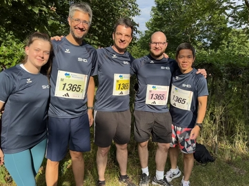 Fünf Personen in SHD-T-Shirts posieren lächelnd vor grüner Kulisse nach einem Lauf.