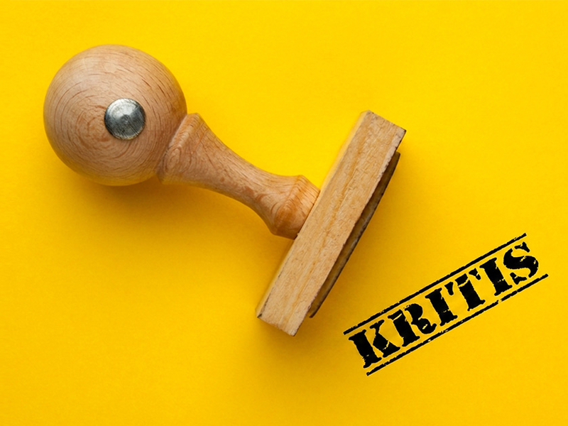 Holzstempel mit dem Aufdruck "KRITIS" vor gelbem Hintergrund, symbolisiert die neue Gesetzgebung für KRITIS-Unternehmen.