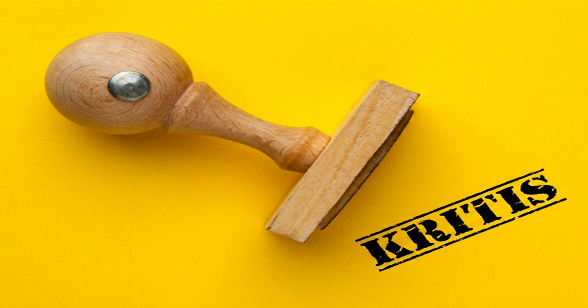 Holzstempel mit dem Aufdruck "KRITIS" vor gelbem Hintergrund, symbolisiert die neue Gesetzgebung für KRITIS-Unternehmen.