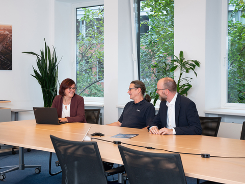 Drei IT-Experten sitzen an einem Tisch, diskutieren IT-Lösungen von SHD in einem modernen Büro.