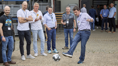 Mann kickt einen Fußball, umgeben von Kollegen, bei einem SHD Event im Freien.