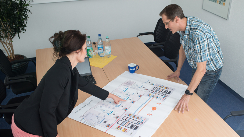 Zwei Personen besprechen einen IT-Plan im Besprechungsraum der SHD, um Lösungen zu entwickeln.