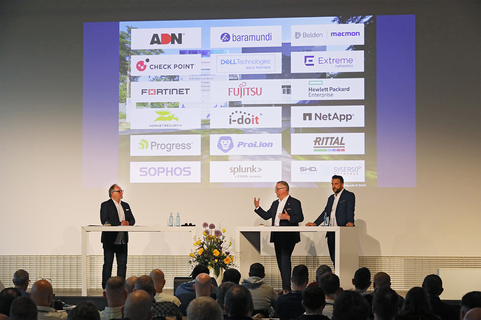 Drei Herren diskutieren über IT-Lösungen vor einer Präsentation verschiedener Technologie-Partner, inklusive SHD.