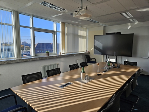 Moderne Konferenzraum mit großem Tisch, Fernseher und Fenster, ideal für SHD Meetings in Berlin.