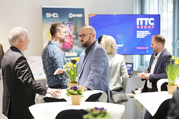 Geschäftsleute diskutieren an Stehtischen bei einer Veranstaltung, präsentiert von SHD und ITTC Group.