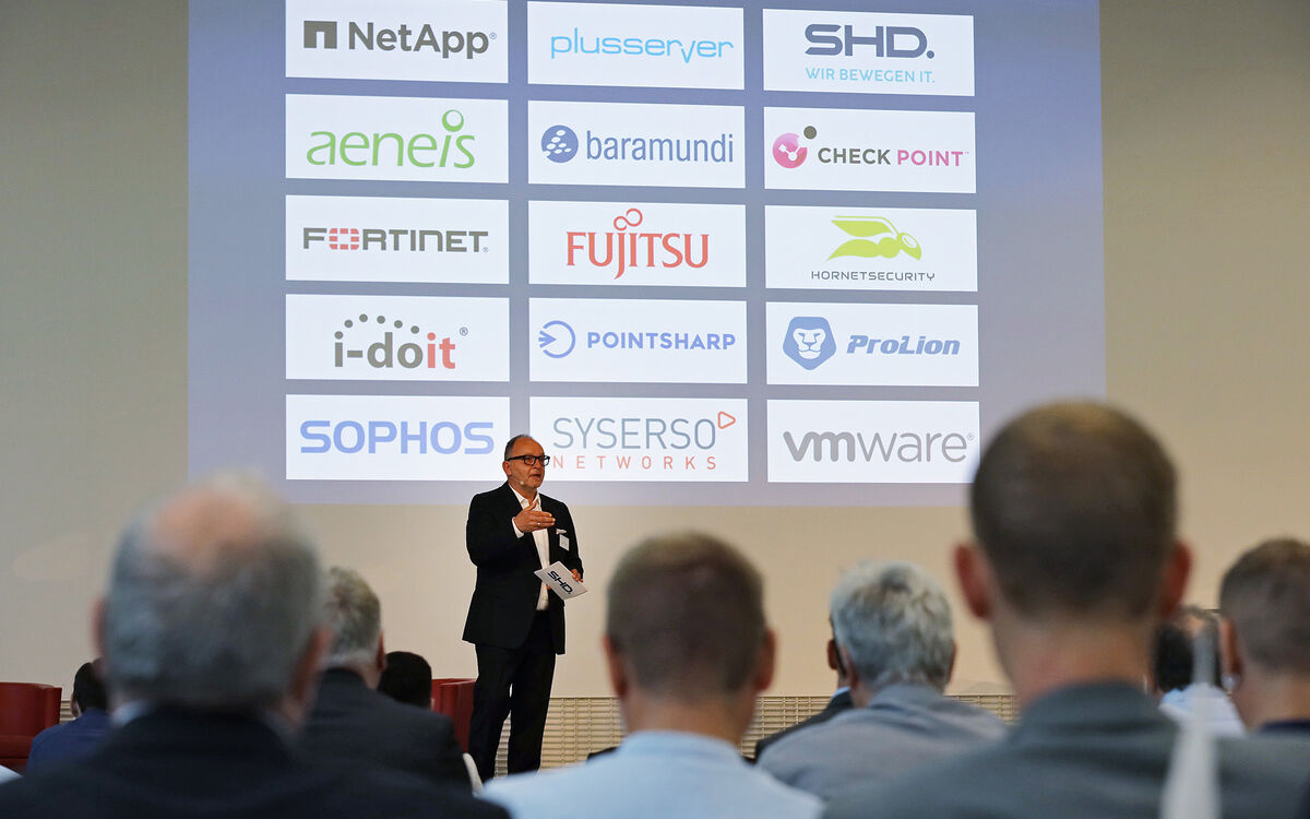 Ein Redner präsentiert IT-Lösungen von SHD und Partnern vor einem Publikum in einem Konferenzraum.