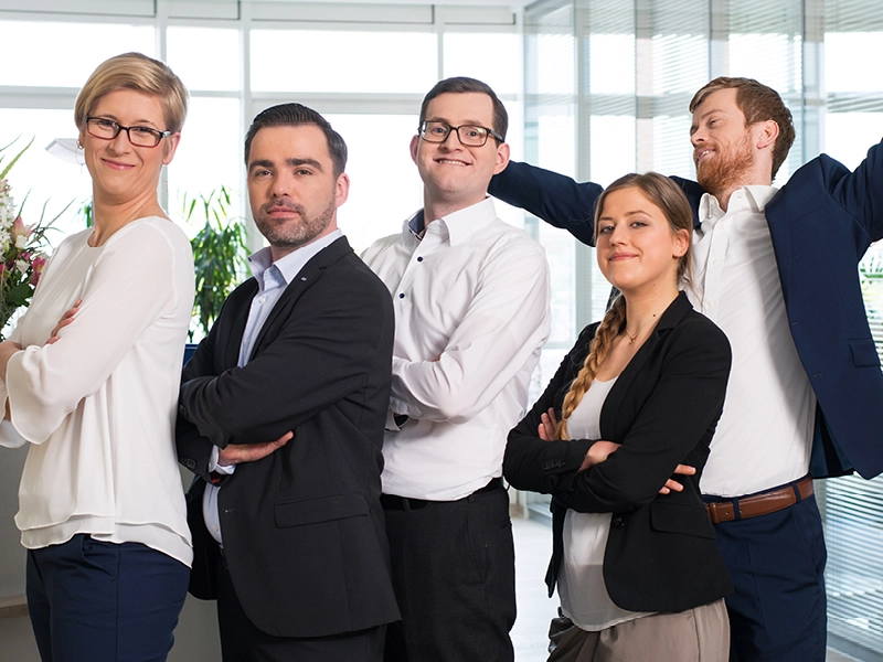 Lächelnde Mitarbeitende von SHD in einer Reihe schauen in die Kamera, einer streckt sich fröhlich