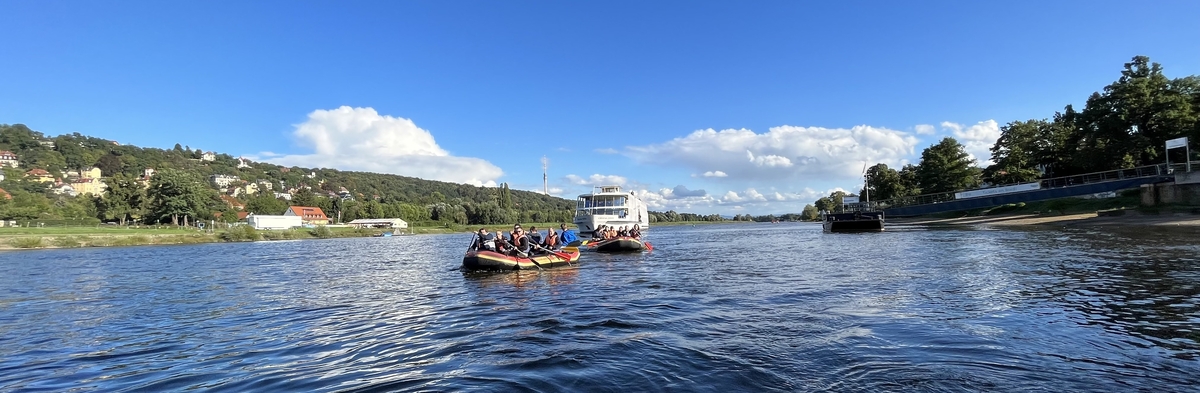 Zwei Booten mit Menschen paddeln auf einem ruhigen Fluss, umgeben von grüner Landschaft. SHD optimiert digitale Erlebnisse.