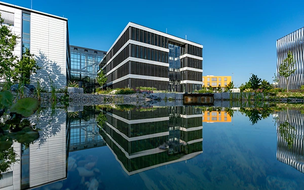 Moderne Bürogebäude reflektieren sich im klaren Wasser, umgeben von gepflegten Grünflächen.