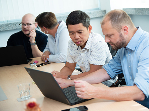 Vier Kolleginnen und Kollegen bei SHD arbeiten gemeinsam an einem Konferenztisch mit ihren Laptops.