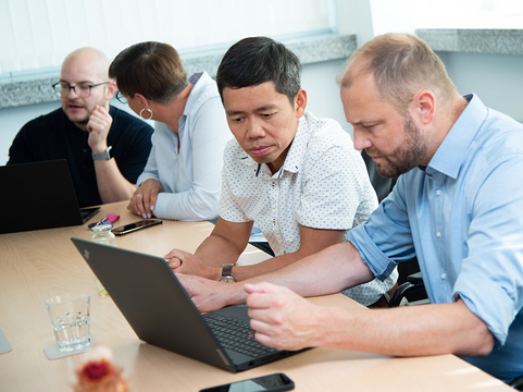 Vier Kolleginnen und Kollegen bei SHD arbeiten gemeinsam an einem Konferenztisch mit ihren Laptops.