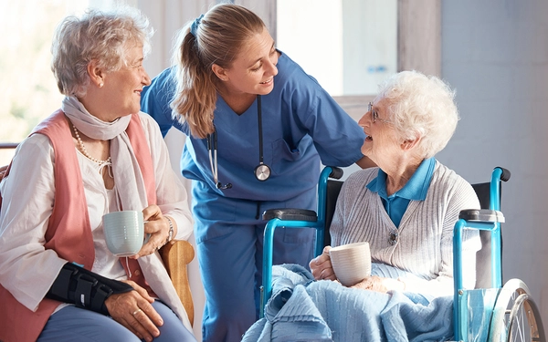 Zwei ältere Damen unterhalten sich lächelnd mit einer Pflegekraft in einem freundlichen Raum. SHD bietet IT-Lösungen für die Pflegebranche an.