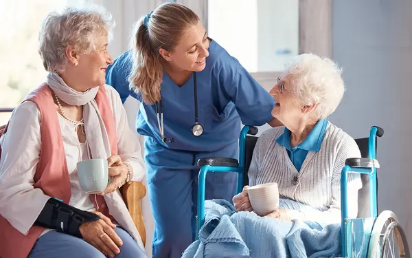 Zwei ältere Damen unterhalten sich lächelnd mit einer Pflegekraft in einem freundlichen Raum. SHD bietet IT-Lösungen für die Pflegebranche an.