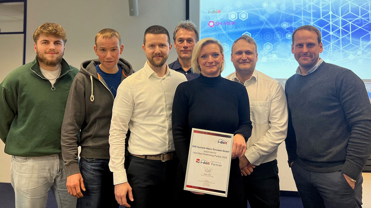 Gruppe von SHD System-Haus-Dresden Mitarbeitern zeigt stolz ihre i-doit Partnerauszeichnung 2024 in einem modernen Raum.