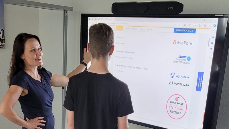 Frau erklärt IT-Lösungen am interaktiven Bildschirm einem Jugendlichen in einem modernen Büro. SHD.