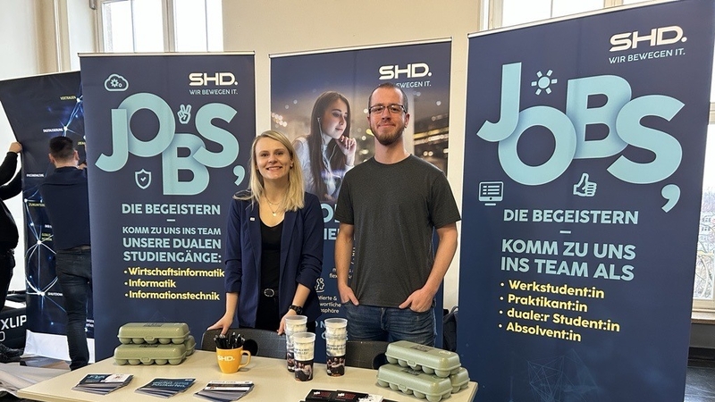 Zwei Mitarbeiter von SHD stehen an einem Messestand und informieren über Jobangebote und duale Studiengänge.