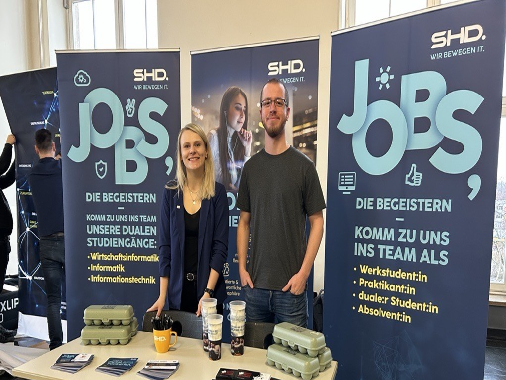 Zwei Mitarbeiter von SHD stehen an einem Messestand und informieren über Jobangebote und duale Studiengänge.