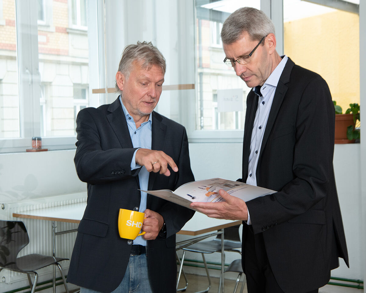 Zwei Männer diskutieren bei SHD, während sie ein Dokument in einem modernen Büro betrachten.