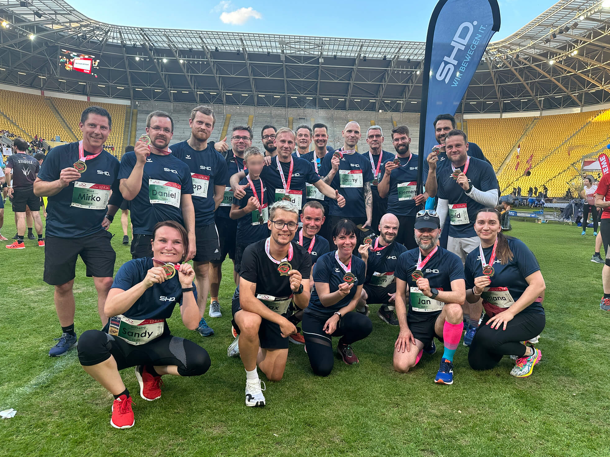 SHD-Team feiert nach dem Lauf im Stadion mit Medaillen, umgeben von jubelnder Atmosphäre.