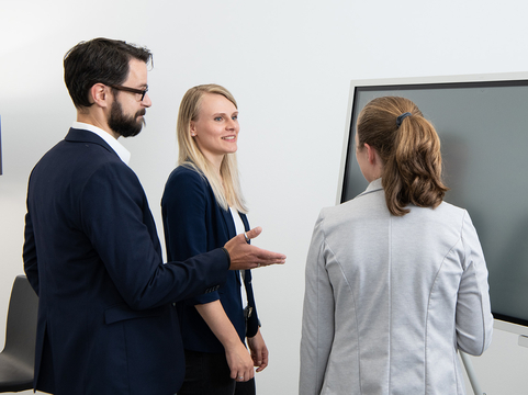 Drei Personen diskutieren lebhaft vor einem interaktiven Bildschirm in einem modernen Büro. SHD bietet innovative IT-Lösungen.