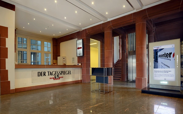Edler Empfangsbereich des SHD Kunden "Tagesspiegel" mit Informationsschalter, Aufstieg zur Treppe und digitalen Anzeigen.