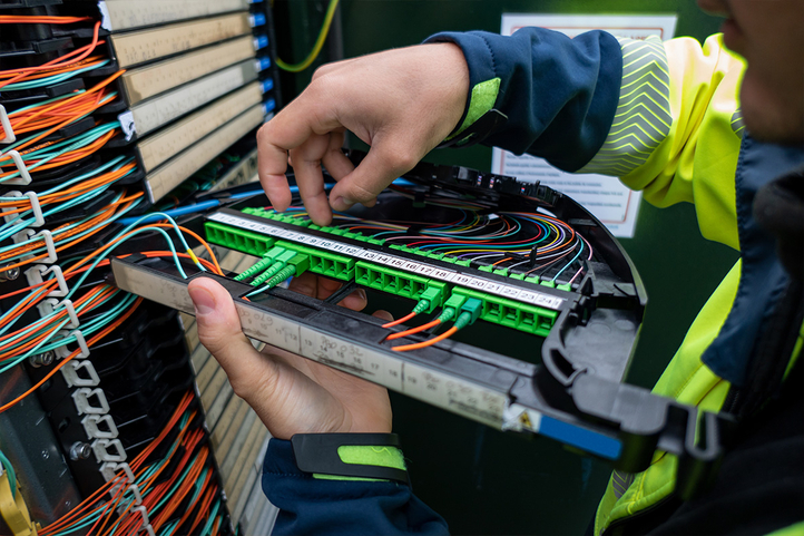 Ein Techniker arbeitet an der Verkabelung innerhalb eines Schaltkastens. Zahlreiche bunte Kabel verlaufen von zahlreichen Anschlüssen.