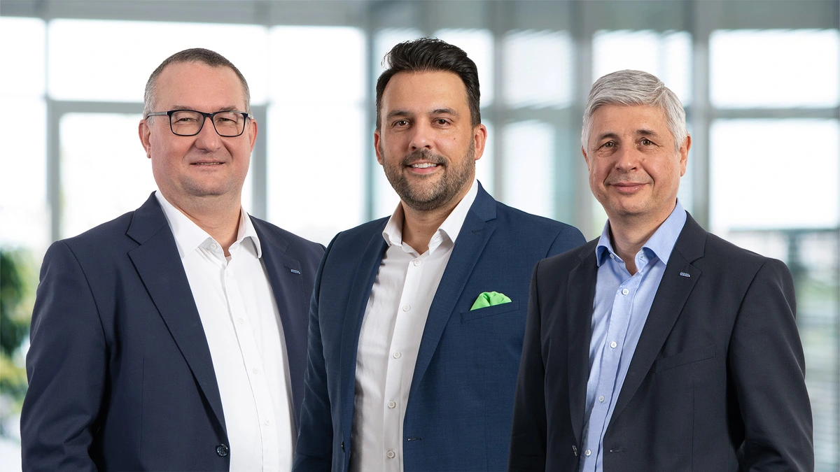 Drei Geschäftsleute posieren freundlich in einem modernen Büro, repräsentieren SHD und IT-Lösungen.