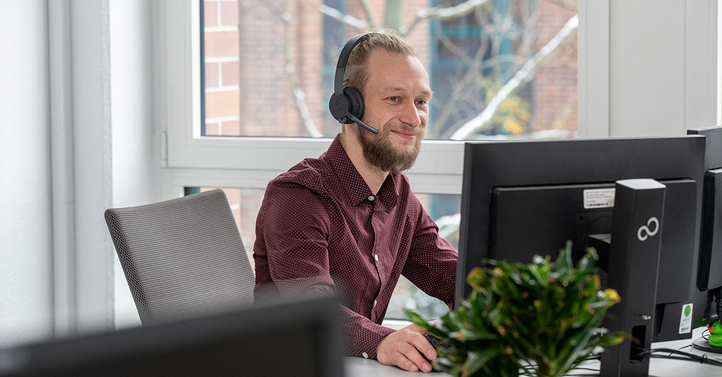 Ein IT-Mitarbeiter berät lächelnd am Computer, während er Kundenservice für SHD bietet.