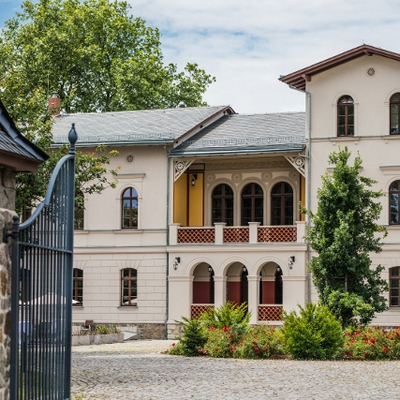Außenaufnahme des Herrenhaus Möckern in Leipzig. Wir blicken durch das offene Eingangstor auf eine helle Hausfassade mit großen Fenstern und einladender Loggia.