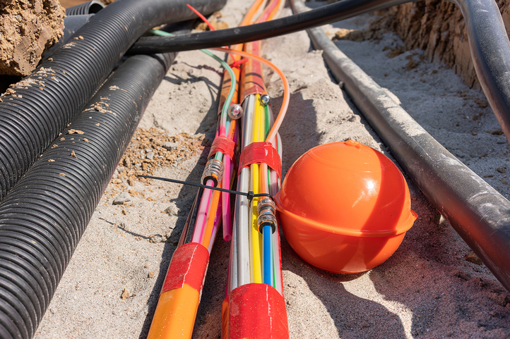 Mehrere Bündel mit Glasfaserkabeln verlaufen innerhalb einer offenen Baustelle. Sie sind von weiteren Rohren und Kabeln umgeben.