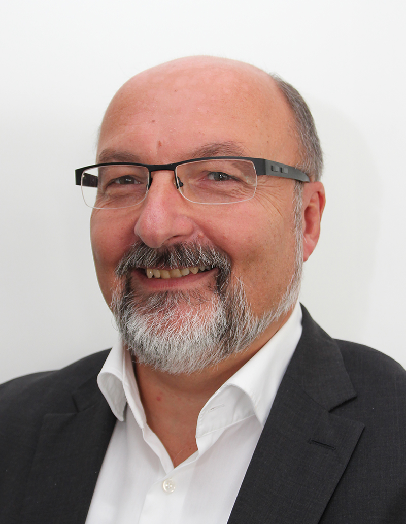 Professioneller Mann mit Brille lächelt, vor neutralem Hintergrund, repräsentiert NetApps Partnerschaft mit SHD.