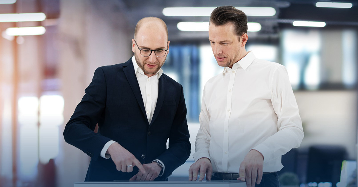 Ein Service Manager von SHD berät einen Kunden im weißen Hemd, beide schauen auf ein Dokument vor ihnen.