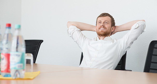 Ein Mann sitzt entspannt an einem Tisch in einem modernen Konferenzraum, lächelnd.